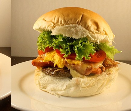 Lanche da Maí Lanches servido no pão de hambúrguer, com alface, tomate, ovo e bacon